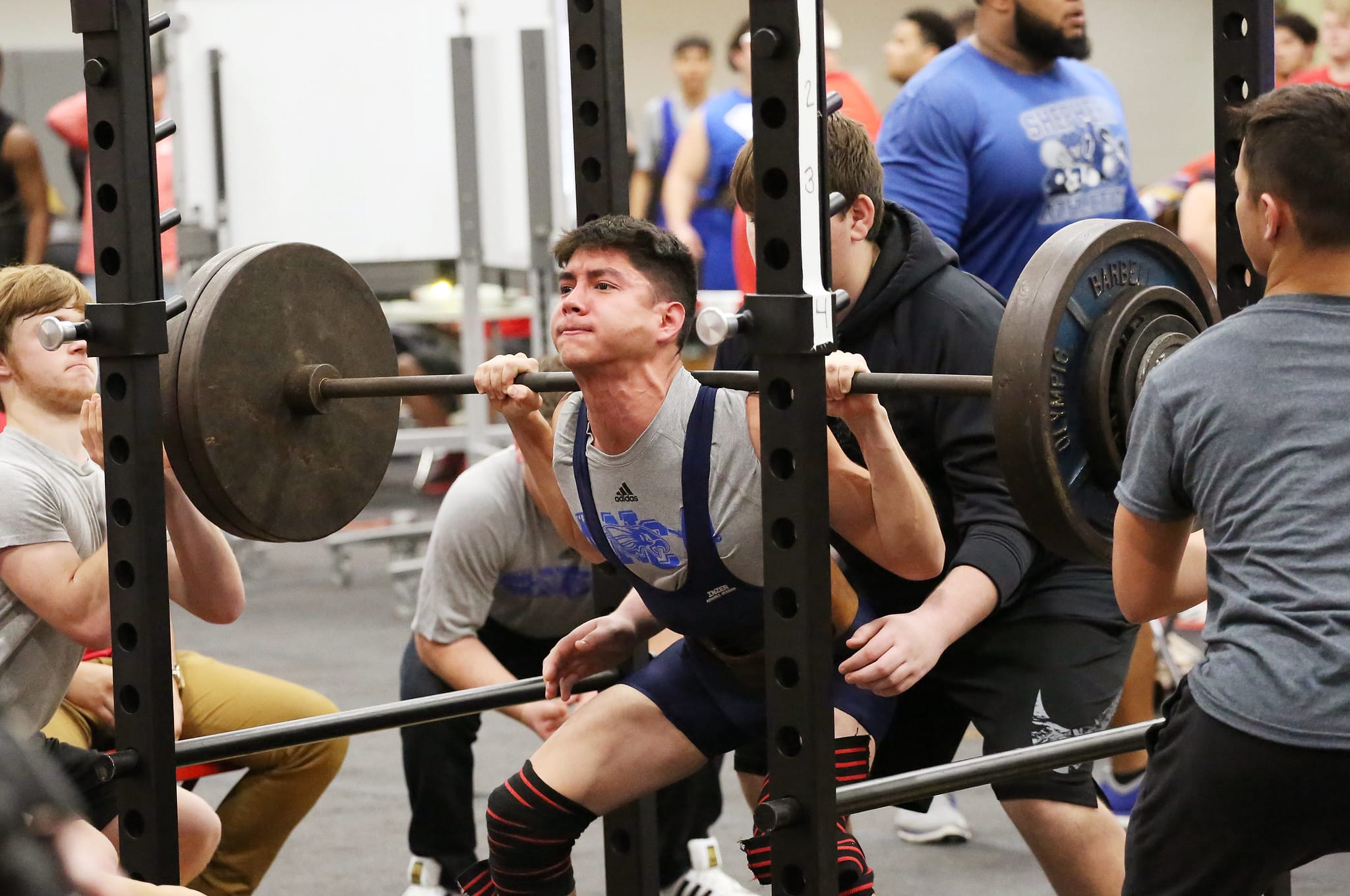 man squatting in a power rack with three spotters