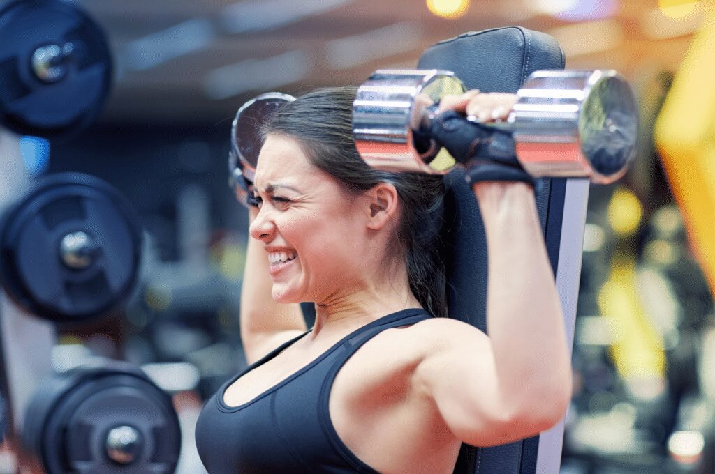 woman pushing one more hard rep in dumbbell overhead press